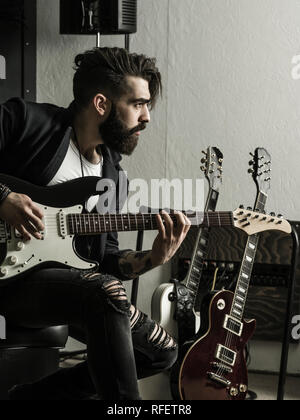 Photo d'un homme à barbe assis et jouant de sa guitare électrique dans un studio d'enregistrement. Banque D'Images