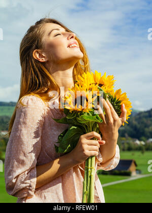 Photo d'un happy young woman holding sunflowers in the sunshine. Banque D'Images