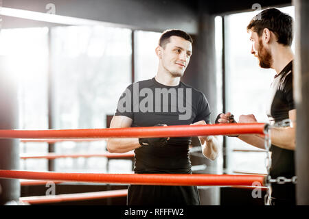 Deux hommes en noir sportswear apprendre à fort sur le ring de boxe à la salle de sport Banque D'Images