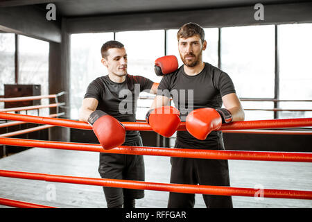 Portrait de deux hommes en noir sport sportswear pendant la pause sur le ring de boxe à la salle de sport Banque D'Images