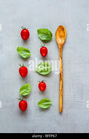 Mise en page créative faite de cuillère en bois, feuilles de basilic et de tomates cerises sur fond clair. Ingrédients de cuisine saine. Concept alimentaire. Télévision lay, top vie Banque D'Images