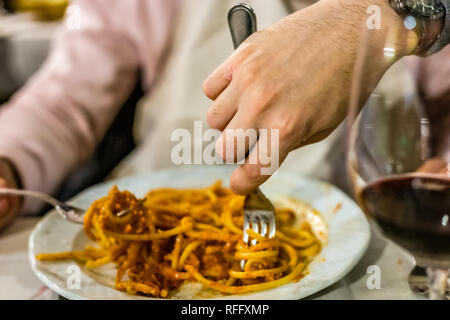 Main de l'homme goûter des nouilles avec sauce typiquement italien à partir de la lave d'un autre diner au restaurant Banque D'Images