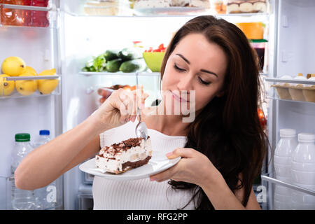 Close-up of a Woman Eating Cake à proximité de réfrigérateur Banque D'Images