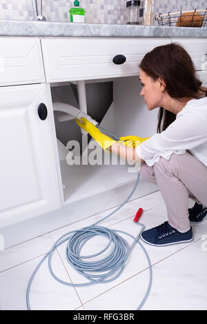 Vue latérale d'une jeune femme en train de nettoyer le tuyau de l'évier bouché dans la cuisine Banque D'Images