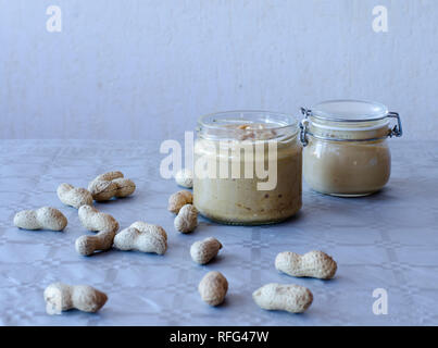 Beurre de cacahuète fait maison dans un bocal en verre avec des cacahuètes réparties sur la table Banque D'Images