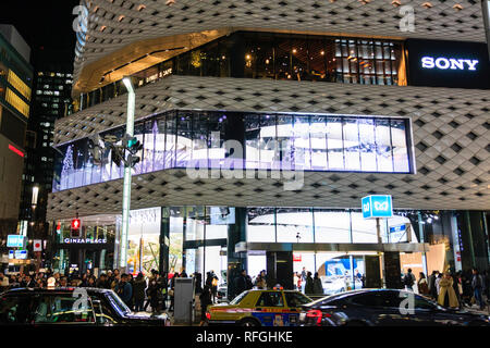 De près de l'édifice Place Ginza blanc avec façade en aluminium bleu pendant l'heure. Allumé. Premier plan, rue avec le trafic passé. Banque D'Images