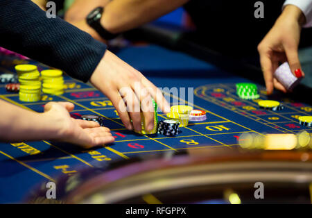 Table de roulette avec des mains de poser des jetons dans un casino. La roue de roulette à l'avant-plan. Jouer jeu. Les gens méconnaissables. Banque D'Images