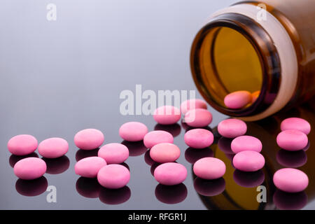 Pilules roses et un flacon en verre brun noir isolé sur une surface réfléchissante. L'industrie pharmaceutique mondiale pour des milliards de dollars par année. D pharmaceutique Banque D'Images