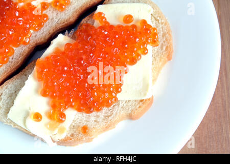 Deux sandwiches avec du beurre et du caviar de saumon sur pain blanc se trouve sur la plaque ronde blanche sur fond de bois Vue de dessus Banque D'Images