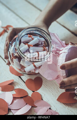 Lover's day. Pot en verre d'ouverture ou de date et désirs ou souhaits. Coeurs en papier rouge à l'arrière-plan. Banque D'Images