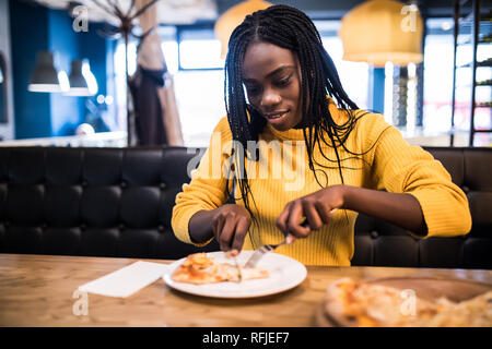 Jeune fille africaine dans chandail jaune pizza manger au restaurant. Banque D'Images