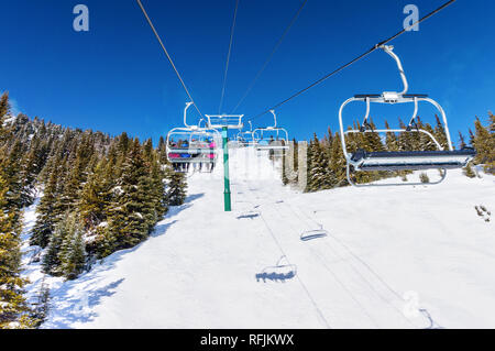 Les skieurs non identifiables sur télésiège remontant une pente de ski dans la montagne enneigée (éventail des Rocheuses canadiennes. Banque D'Images