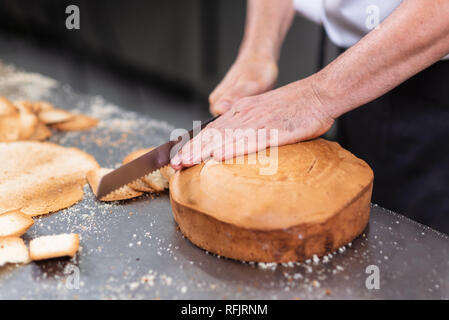 Chef pâtissier de couper le gâteau éponge sur couches. Processus de la production de gâteaux . Banque D'Images