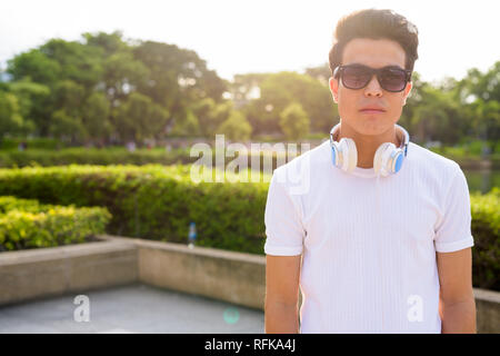 Young Asian man wearing headphones tout en vous relaxant dans le parc Banque D'Images