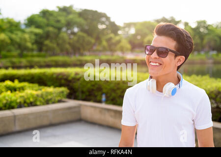 Young Asian man wearing headphones tout en vous relaxant dans le parc Banque D'Images