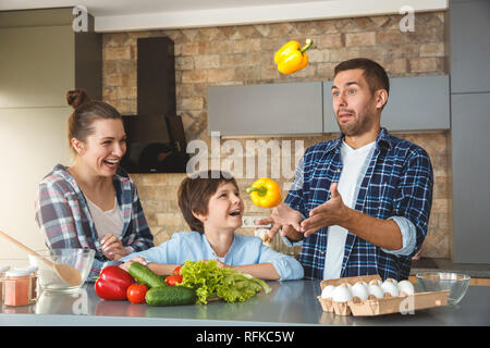 Famille à la maison debout dans la cuisine ensemble, la mère et le fils à la jonglerie au père rire joyeux Banque D'Images