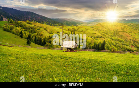 Hay shed sur un terrain herbeux en montagne. une campagne magnifique paysage de printemps au coucher du soleil dans la lumière du soir. Nuageux l'après-midi. village sur la di Banque D'Images