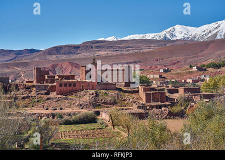 Le village traditionnel en briques de boue abrite la mosquée. Les montagnes enneigées de l'Atlas sont à l'arrière. Pris près d'Ighrem n'Ougdal, province d'Ouarzazate, Maroc Banque D'Images