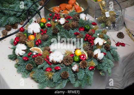 Couronne de Noël Atelier de tissage. Femme de couronnes de décoration mains faites de branches d'épinette, cônes et diverses décorations organique sur la table Banque D'Images