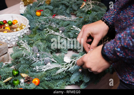 Couronne de Noël Atelier de tissage. Femme de couronnes de décoration mains faites de branches d'épinette, cônes et diverses décorations organique sur la table Banque D'Images