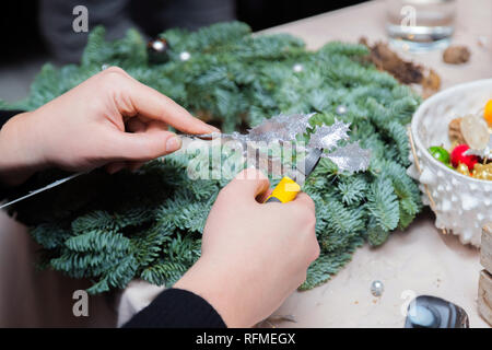 Couronne de Noël Atelier de tissage. Femme de couronnes de décoration mains faites de branches d'épinette, cônes et diverses décorations organique sur la table Banque D'Images