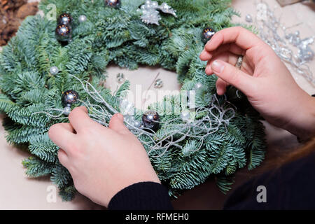 Couronne de Noël Atelier de tissage. Femme de couronnes de décoration mains faites de branches d'épinette, cônes et diverses décorations organique sur la table Banque D'Images