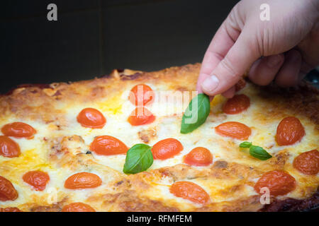 Woman decorating lasagnes végétariennes aux herbes dans la plaque de cuisson qui vient d'être pris hors du four Banque D'Images