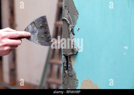 La main libre de constructeur ciment colle des traînées sur le mur avec une truelle pour coller des carreaux de céramique dans la salle de bains. Concept Rénovation Réparation, révision, d'un contrat Banque D'Images