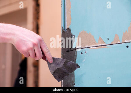 La main libre de constructeur ciment colle des traînées sur le mur avec une truelle pour coller des carreaux de céramique dans la salle de bains. Concept Rénovation Réparation, révision, d'un contrat Banque D'Images