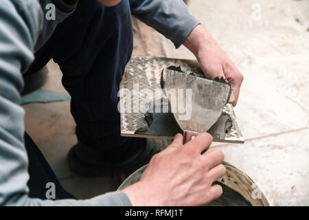 La main libre de constructeur ciment colle sur le frottis en carreaux de céramique avec une truelle pour colle dans la salle de bains privative. Concept Rénovation Réparation, révision, contrat carreleur Banque D'Images