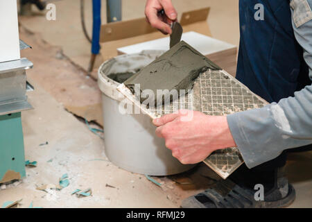 La main libre de constructeur ciment colle sur le frottis en carreaux de céramique avec une truelle pour colle dans la salle de bains privative. Concept Rénovation Réparation, révision, contrat carreleur Banque D'Images