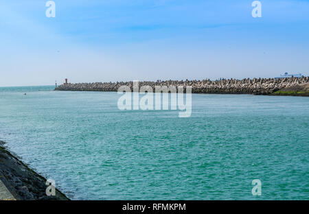 Vue sur l'estuaire de la rivière vers la mer, brise-lames en béton et les gens au loin. Banque D'Images