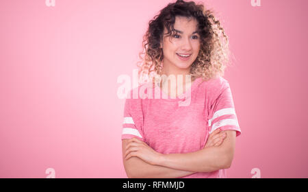 Portrait de jeune fille gaie belle avec des cheveux bouclés et lâche t-shirt rose isolé sur fond rose, pour femme, Texte et concept emotio Banque D'Images