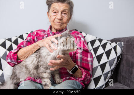Très vieux portrait grand-mère avec les cheveux gris et les rides profondes est assis à la maison sur le canapé en jeans et une chemise à carreaux rouge avec un gris Banque D'Images