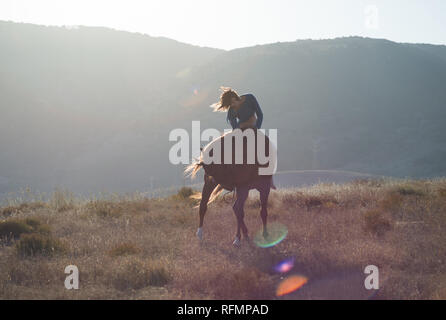 Une fille à cheval dans un champ représentant le mouvement harmonieux corps et cheveux avec des reflets et rural voir l'arrière-plan Banque D'Images