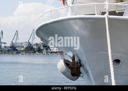 Close up de grand bateau blanc avec ancre et côté mer corde contre port industriel avec des grues et docks contexte hors foyer à Varna, Bulgarie. Banque D'Images