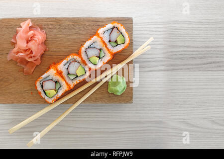 Petits pains à sushis Maki avec baguettes sur une assiette en bois avec wasabi et gingembre mariné. Vue de dessus du restaurant sushi, isolé sur fond de bois gris. Banque D'Images