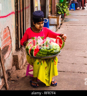 Femme portant Thanaka birman pâte cosmétique sur son visage assis sur le trottoir, la vente de tranches de melon d'eau Banque D'Images