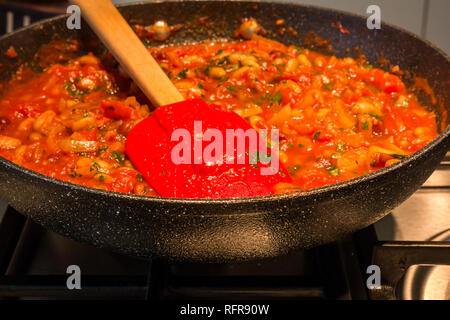 Close up Préparation du ragoût italien avec des tomates, haricots, herbes et sauce à l'oignon dans une poêle avec un anneau sur le gaz traité spatule Banque D'Images