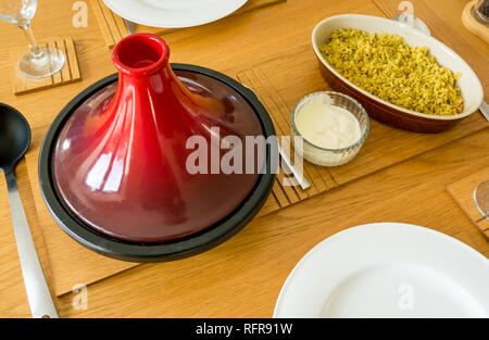 Céramique rouge et fonte tagine sur table en chêne avec des poches, couscous, des yaourts et de la vaisselle blanche Banque D'Images