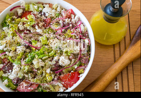 Vaisselle blanche saladier rempli de salade grecque avec fromage feta, tomates, oignons rouges, avocat, laitue et vinaigrette de citron dans un bocal en verre Banque D'Images