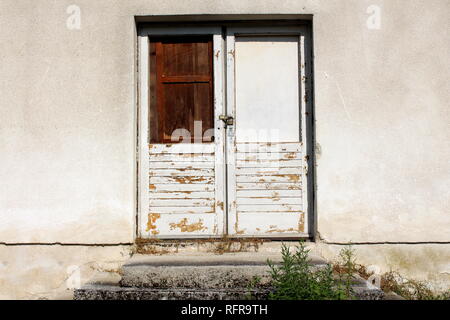 Verrouillé les portes en bois blanc craquelé, peinture en mauvais état avec des fenêtres cassées remplacées par des commissions scolaires et cadenas rouillé sur l'ancien mur gris avec des mesures concrètes Banque D'Images