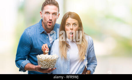 Jeune couple amoureux eating popcorn sur fond isolé en peur avec une surprise de Choc Visage, peur et excité par la peur d'expression Banque D'Images