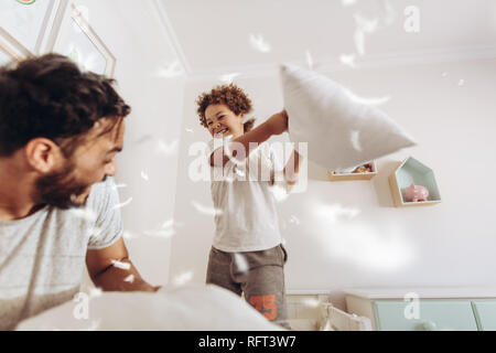 Heureux père et fils d'une guerre d'oreillers sur le lit de plumes voler autour. Père et fils s'amusant de jouer à la maison. Banque D'Images