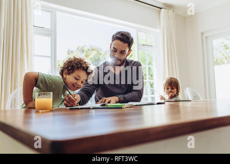 L'homme assis à la table à la maison avec ses enfants en prenant soin d'eux. Père d'aider son fils dans ses études. Banque D'Images