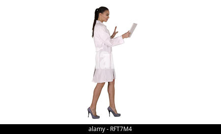 Vue latérale sur toute la longueur. Jeune femme médecin holding tablet dans ses mains et faisant appel vidéo sur fond blanc. Professional tourné en 4K de résolution. 0 Banque D'Images