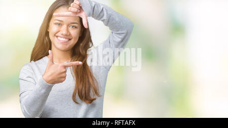 Jeune belle brunette woman wearing sweater sur fond isolé du châssis en souriant avec les mains et les doigts avec un visage heureux. La créativité et le ph Banque D'Images