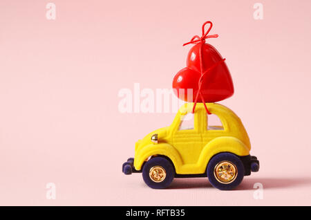 Petite voiture jaune porte un cœur rouge. Le concept de la Saint-Valentin. Banque D'Images