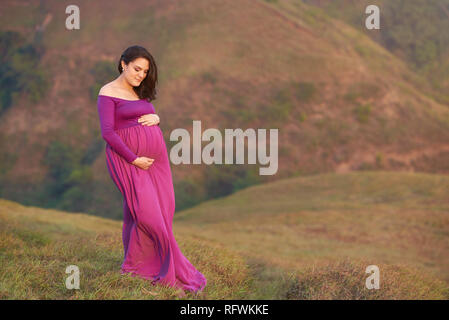 Pregnat woman hugging ventre sur fond naturel Banque D'Images