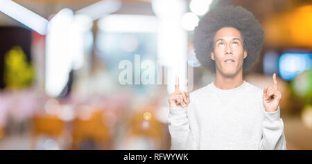 Young african american man with afro hair port sweatshirt sportive dans l'étonnement et la surprise de la recherche de pointe et avec les doigts et les bras levés. Banque D'Images